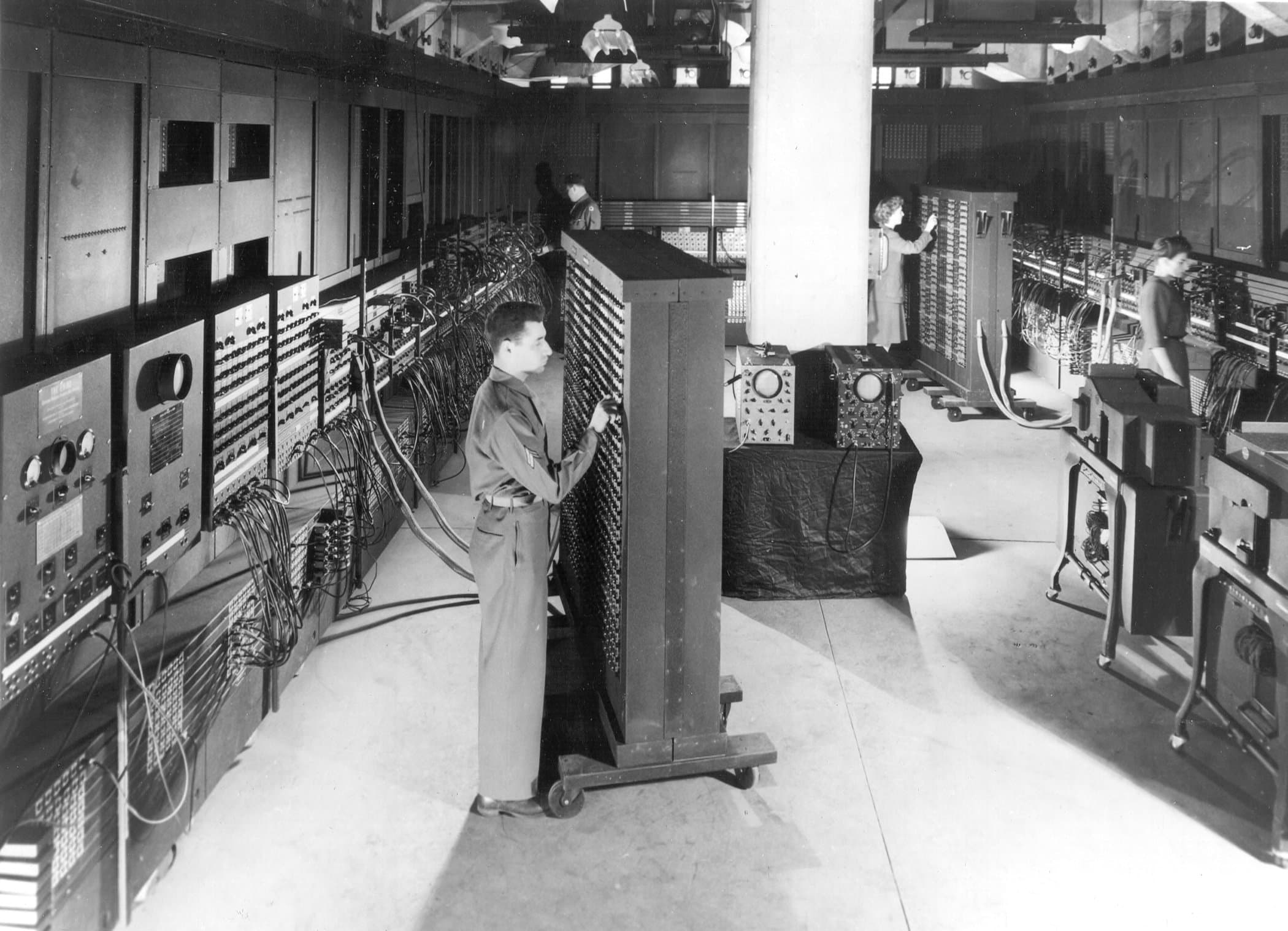 ENIAC, 1946 — Corporal Irwin Goldstein adjusting one of the function tables, dwarfed by the wall of vacuum tubes behind him